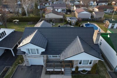 Hy-Grade-Steel-Roofing-System-Metal-Roofing-See-Our-Work-Slate-Grey-large green grass-behind-bungalow-home-with-white siding with beige accents-angle is from above - drone