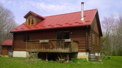 Hy-Grade-Steel-Roofing-System-Metal-Roofing-See-Our-Work-Tile-Red-bungalow-style house-with green grass and blue sky with brown log siding