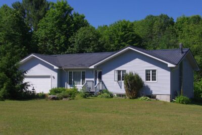 Hy-Grade-Steel-Roofing-System-Metal-Roofing-See-Our-Work-Slate-Grey-wooded-area-Orillia, Ontario green trees behind home with white siding.