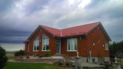Hy-Grade-Steel-Roofing-System-Metal-Roofing-See-Our-Work-Tile-Red-bungalow-style house-with green grass and stormy-grey sky with red brick siding