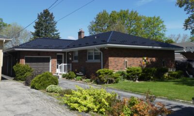 Red brick bungalow can be seen with a Black Hy-Grade Steel roof on a sunny day with blue sky. There are lots of plants and bushes in various colours of green surround the home.