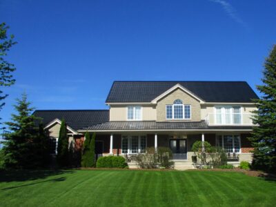 A Hy-Grade metal roof in black from a straight on angle with a sunny blue-sky in the background. The siding of the home is a cream-yellow.