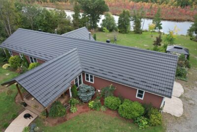 Hy-Grade Steel Roof in Tamworth with bright red brick shot from above with a drone. The backyard can be seen behind and a front yard with green bushes are in the front. A black lab lays by the front door.