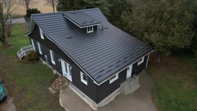 Hy-Grade Steel roof from above on a house with black siding and white accents. A farmer's field can be seen off to the left in the background.