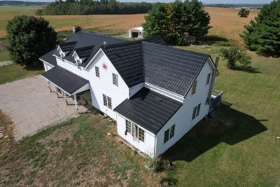 Multi-story House with a Black Hy-Grade Steel roof on a bright sunny day with. the angle is bird's eye from a drone and the brick of the home is a bright white.