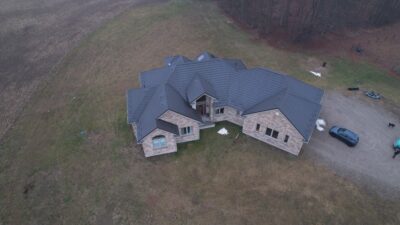 Drone angle with Hy-Grade metal roof in dark brown. Photos taken in spring, ground is still dead from winter. Lots of grass/yard space around the beige bricks