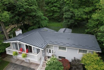 Hy-Grade-Steel-Roofing-System-Metal-Roofing-See-Our-Work-Slate-Grey-large green trees-behind-bungalow-home-with-whitesiding-cottage-style-angle is from above - drone