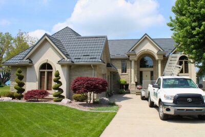Hy-Grade-Steel-Roofing-System-Metal-Roofing-See-Our-Work-Slate-Grey-green-grass-beige-building-Hy-Grade-Steel Roofing Truck-in driveway