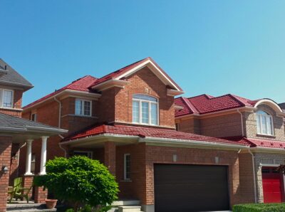 Hy-Grade-Steel-Roofing-System-Metal-Roofing-See-Our-Work-Tile-Red-bungalow-style house-with green grass and blue sky with red brick siding and dark brown coloured garage door.