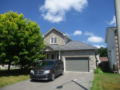 Hy-Grade-Steel-Roofing-System-Metal-Roofing-See-Our-Work-Charcoal-Grey-metal-roof-rural-home-blue-sky-green-grass-in-front-of-home-big-driveway-with-chalk-and-black-minivan-in-driveway