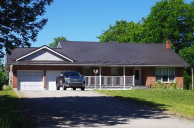 Hy-Grade Steel Roof red-brick House Dark Brown-Roof with long driveway and truck in the middle. Blue sky can be seen in the background