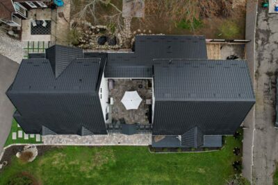 A Hy-Grade steel roof from a bird's eye view can be seen with on a white brick house. Un the middle a yard with a table is seen.