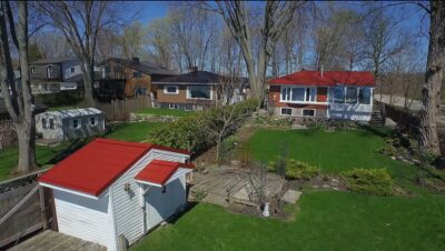 Hy-Grade-Steel-Roofing-System-Metal-Roofing-See-Our-Work-Tile-Red-coottage-style houses- with shed in bottom left corner with green grass and blue sky and multiple houses in the back with steel roofs.