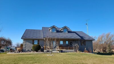 Hy-Grade-Steel-Roofing-System-Metal-Roofing-See-Our-Work-Charcoal-Grey-metal-roof-blue-sky-in-background-beige-bricks-dead-bushes