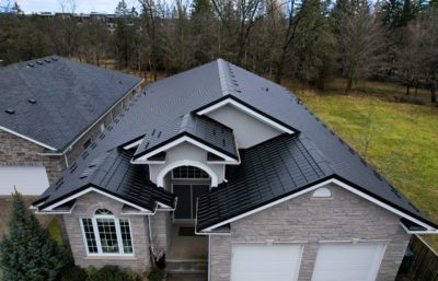 Multi-story House with a Black Hy-Grade Steel roof on a bright cloudy day with. the angle is bird's eye from a drone and the brick of the home is grey