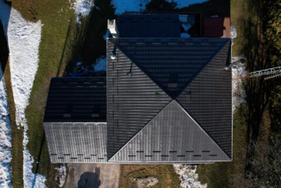 A Hy-Grade steel roof from a bird's eye view can be seen with green grass covered with small patches of snow in the back and front yard.