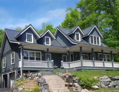 Hy-Grade-Steel-Roofing-System-Metal-Roofing-See-Our-Work-Slate-Grey-wooded-area-blue-siding-white-wrap-around-porch-cobble-staires-up-to-home