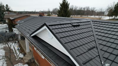 2 story house with a Black Hy-Grade Steel roof on a cloudy day with. the angle is bird's eye from a drone and the brick of the home is red brick.