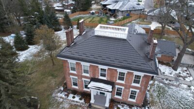 Drone angle with Hy-Grade metal roof in dark brown. The house in colonial stlye, multiple stories and has bright red bricks.