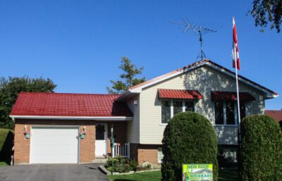 Hy-Grade-Steel-Roofing-System-Metal-Roofing-See-Our-Work-Tile-Red-bungalow style house-with-green-grass-and-blue-sky- Hy-Grade-Steel-Roof-sign-in-bottom-right