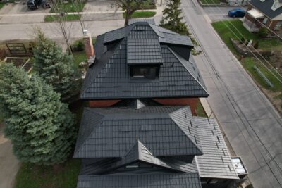 A Hy-Grade steel roof in black from a bird's eye view can be seen with a red brick chimney can be seen on the third level of the home..