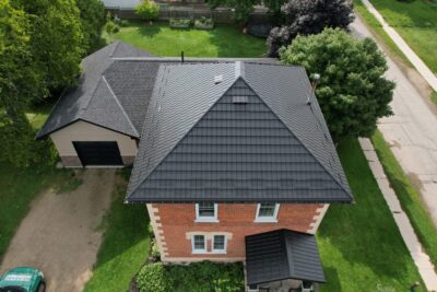 2 story house with a Black Hy-Grade Steel roof on a bright cloudy day with. the angle is bird's eye from a drone and the brick of the home is red brick.